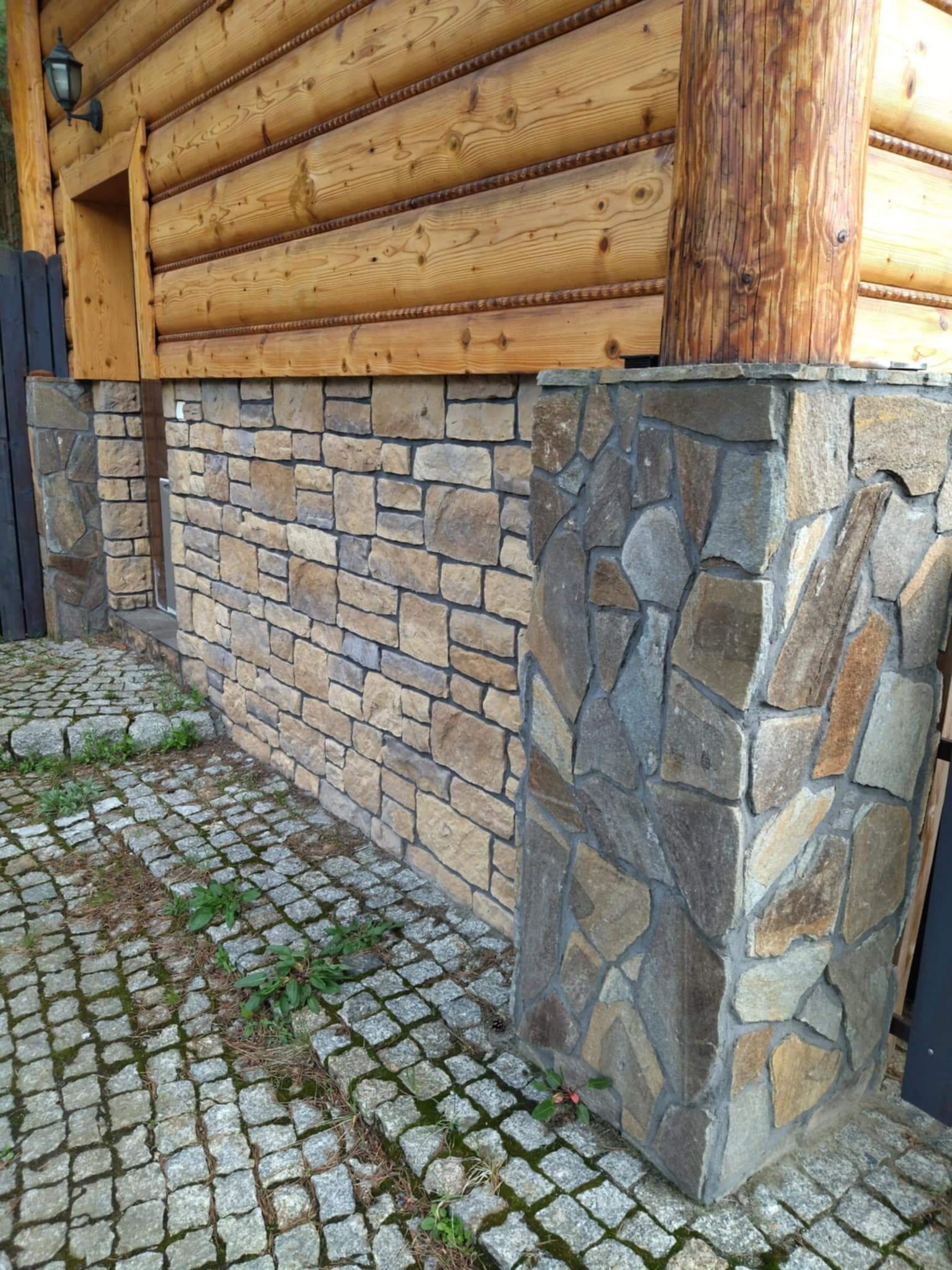 Obraz przedstawia drewniany domek z ładną kamienną podmurówką